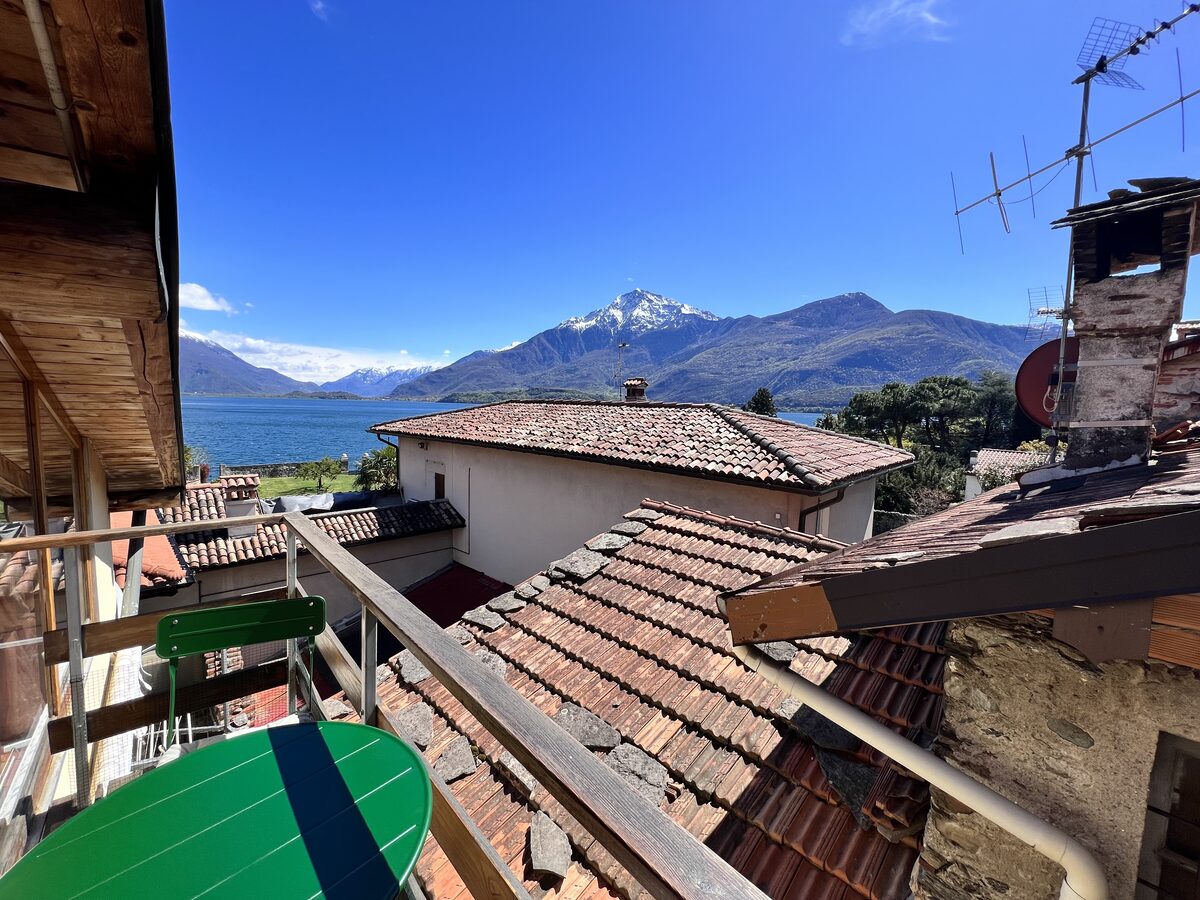 Small balcony with green table and chairs overlooking rooftops, the lake and mountains