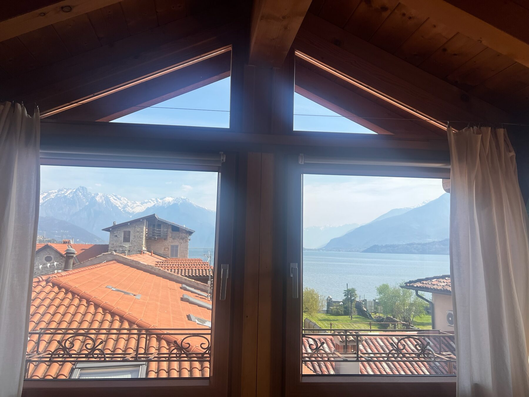 Mansard window of Casa Elenina framing Lake Como and snow-capped mountains